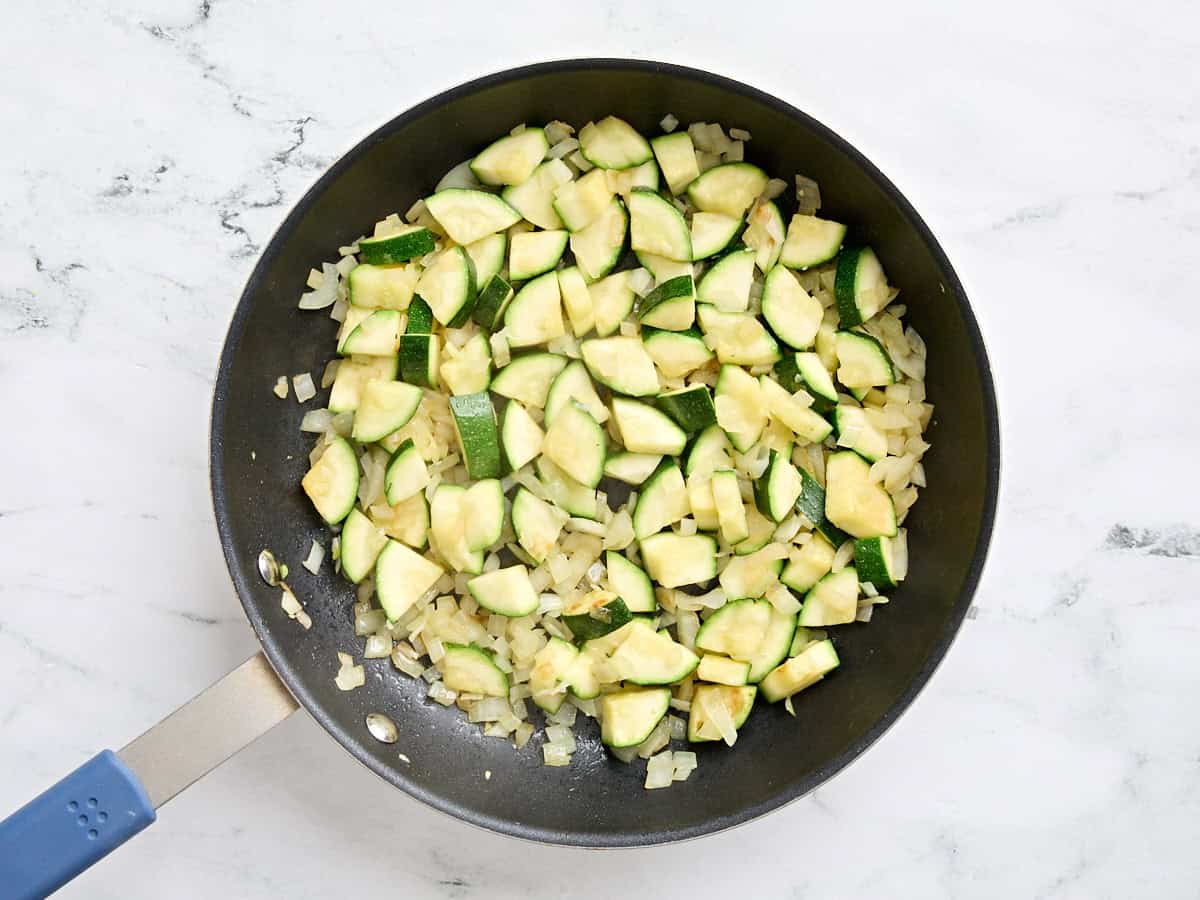 Diced onion and sliced zucchini in a skillet after being sauteed.