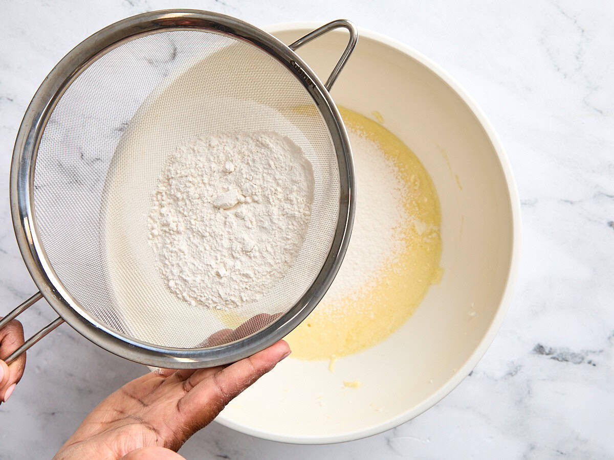 The dry ingredients for coconut cake being sifted into the wet ingredients.