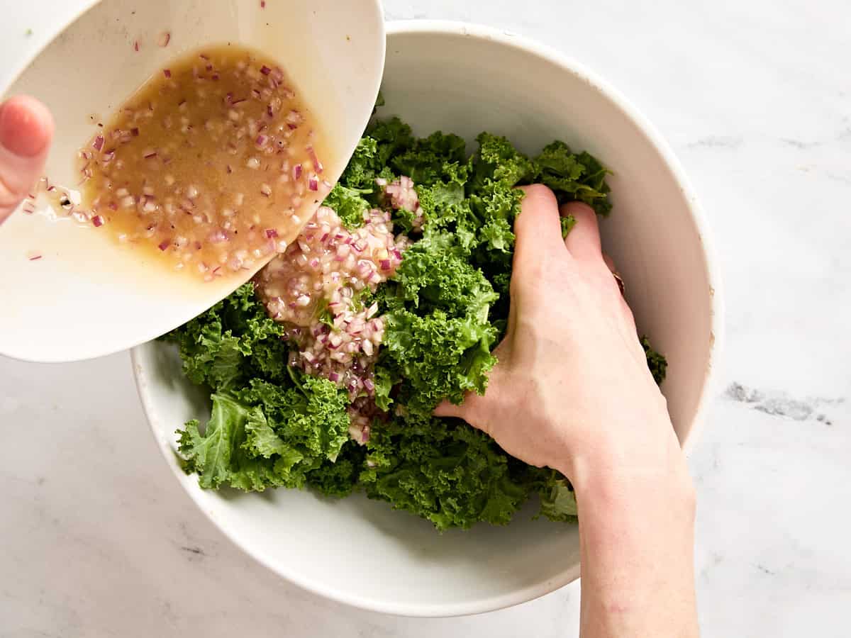 Bacon vinaigrette being massaged into fresh kale.