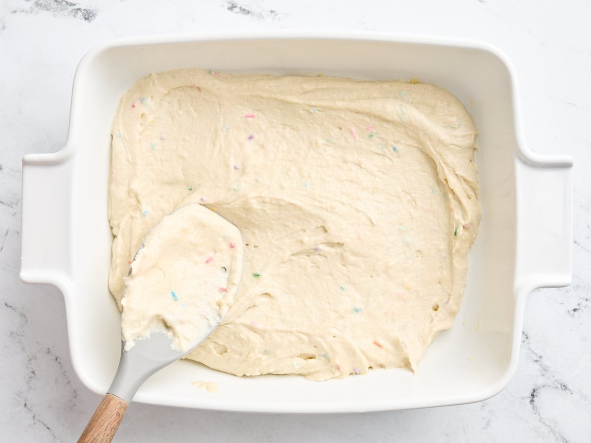 Sugar cookie bar batter being spread into a baking dish.
