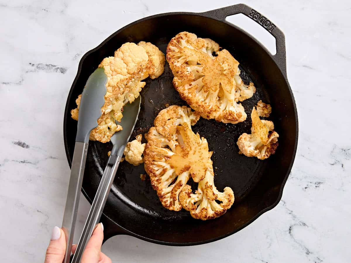 Cauliflower steaks cooking in a skillet.