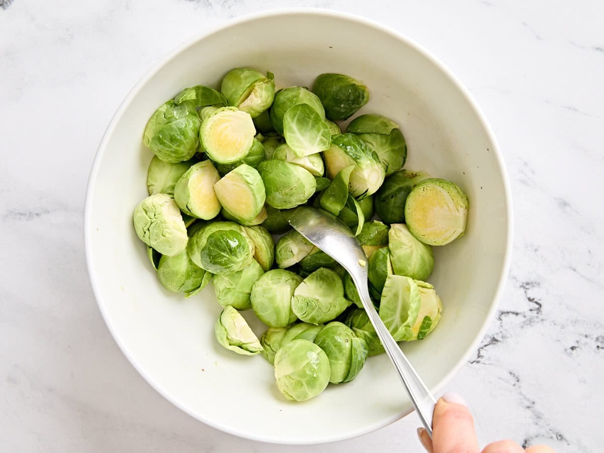 Brussels sprouts in a bowl being tossed in oil.