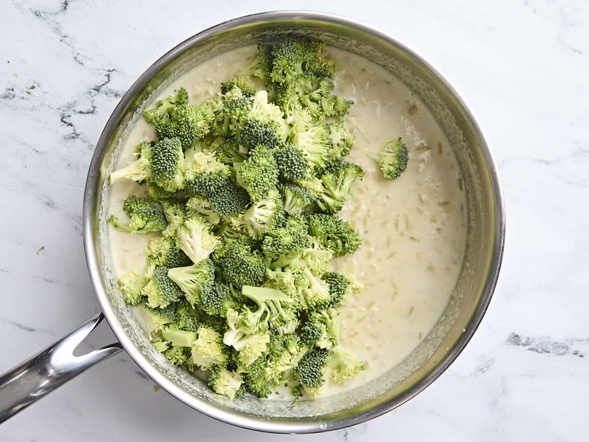 Fresh broccoli florets added to orzo in a creamy sauce in a skillet.