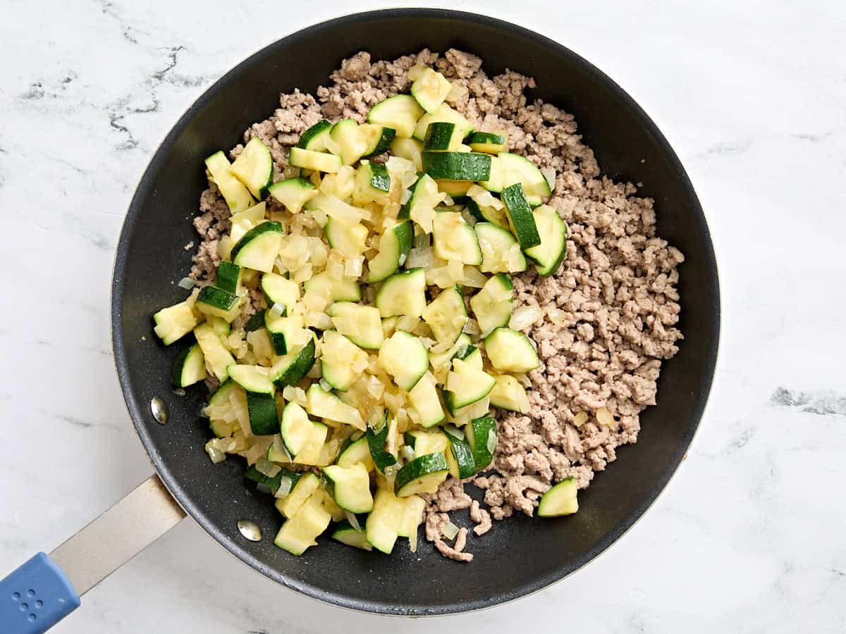 Sauteed zucchini and onion added to browned ground turkey in a skillet.