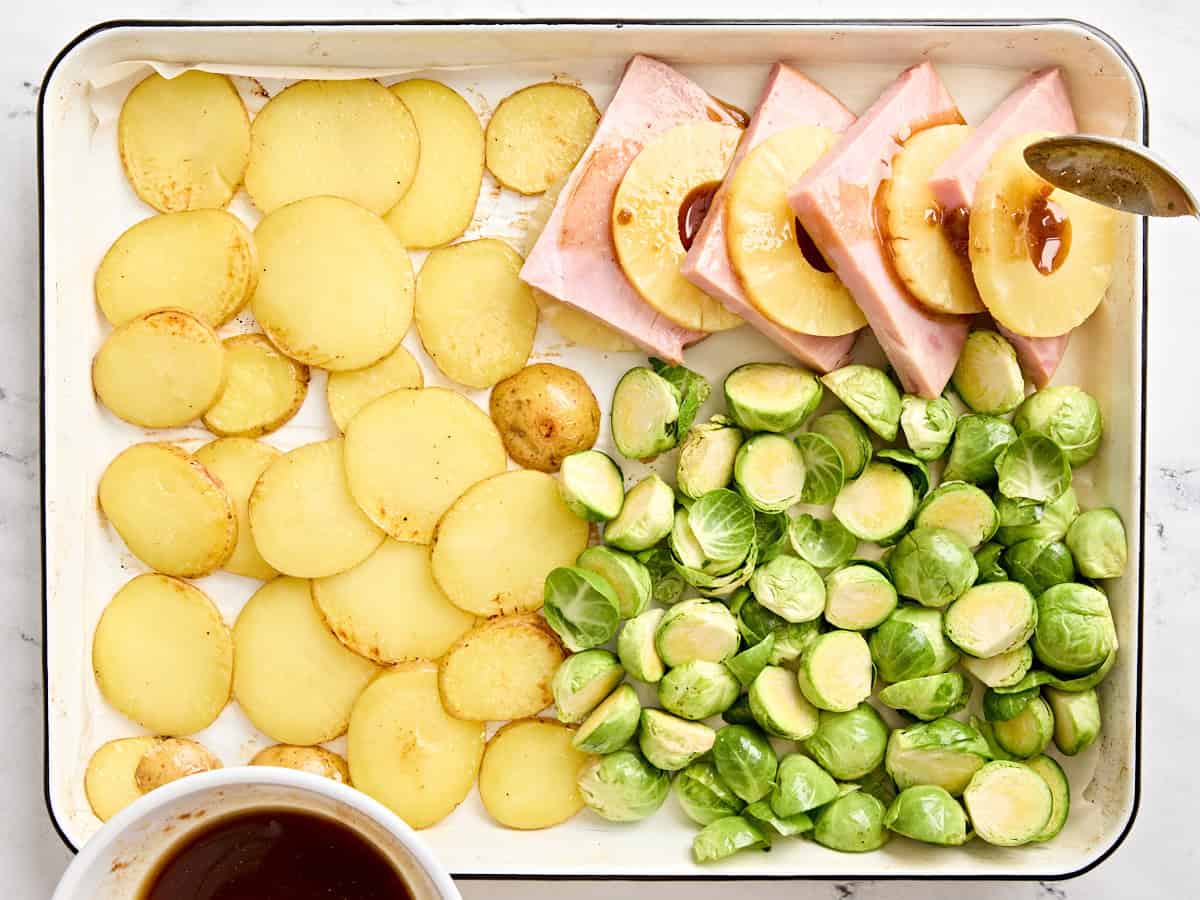 A spoon dripping a glaze onto sliced ham steaks and pineapple rings.