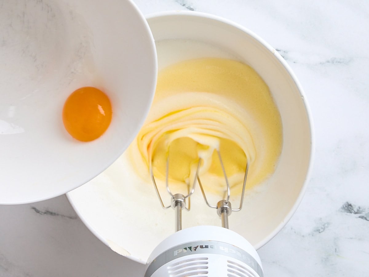 A yolk being poured into whipped egg whites in a bowl.