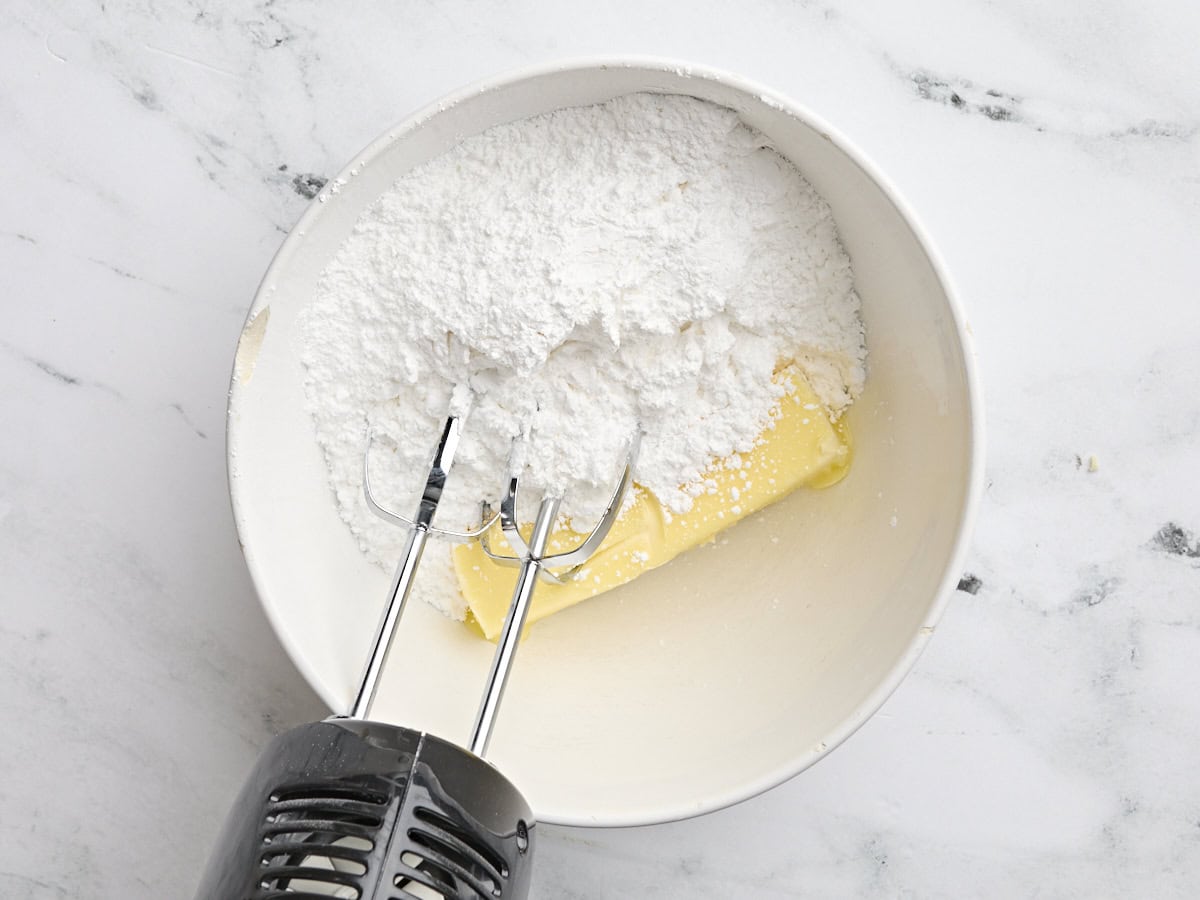 Butter and powdered sugar in a mixing bowl with a hand mixer.