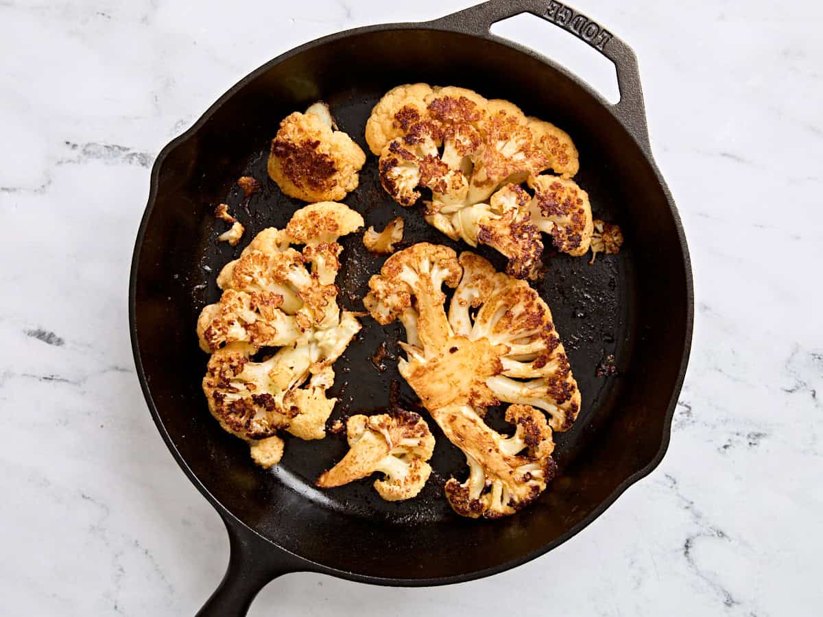 Finished cauliflower steaks in a skillet.
