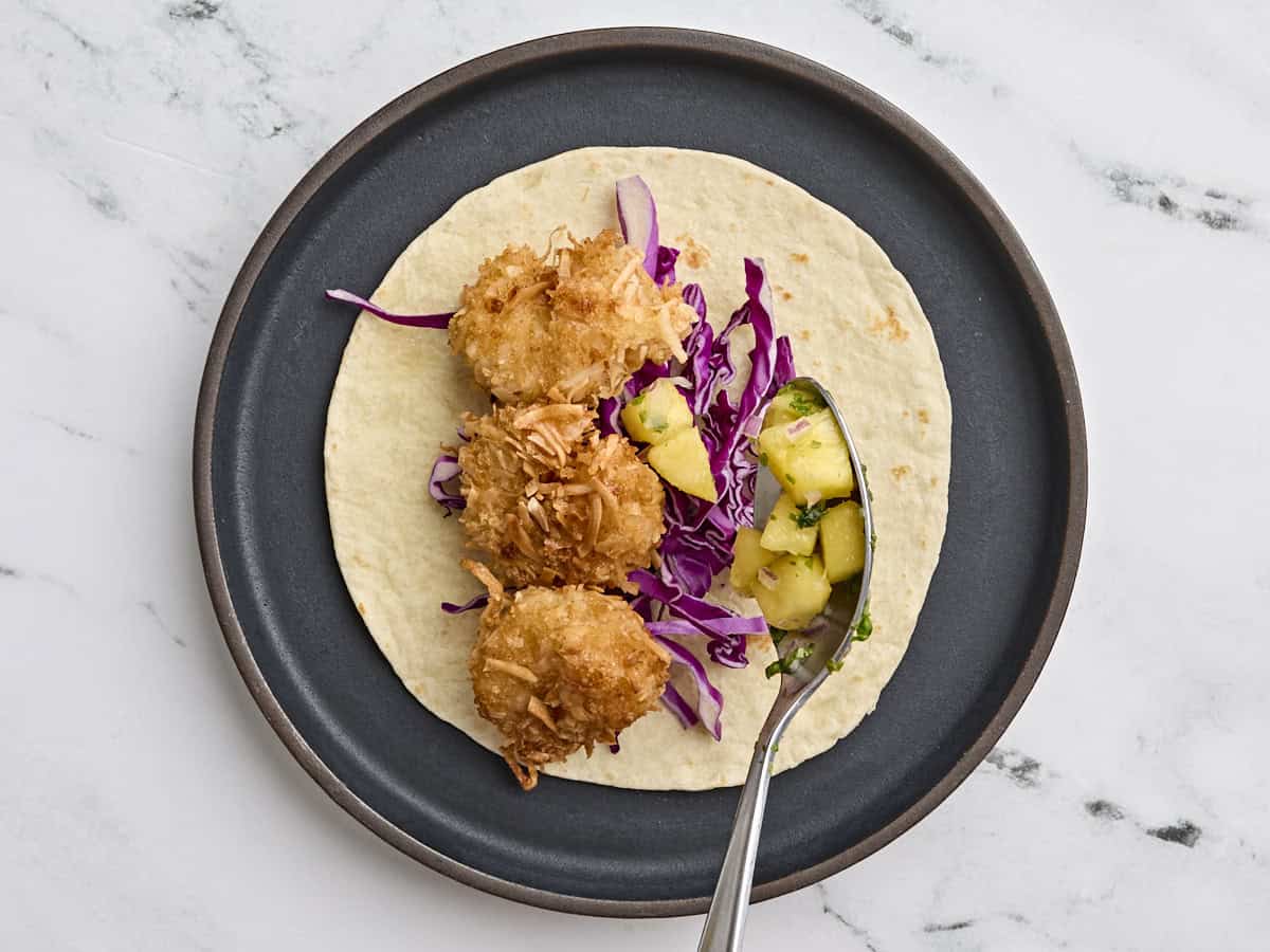 Coconut shrimp on a taco tortilla with shredded cabbage and pineapple salsa.