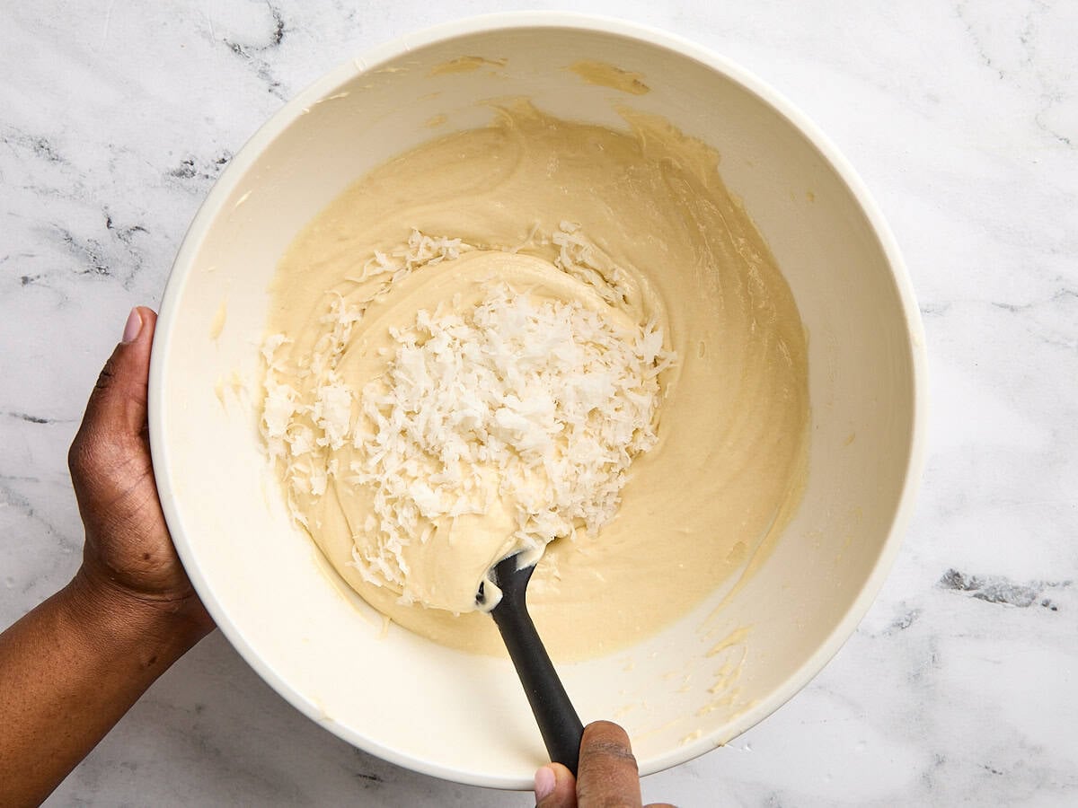Shredded coconut being folded into the batter for coconut cake in a bowl.