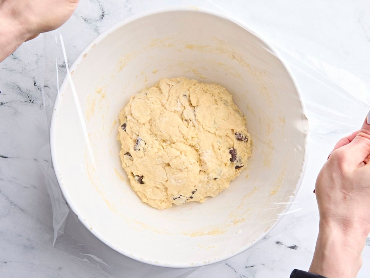 Chocolate chip sourdough scone dough in a mixing bowl, being covered with plastic wrap.
