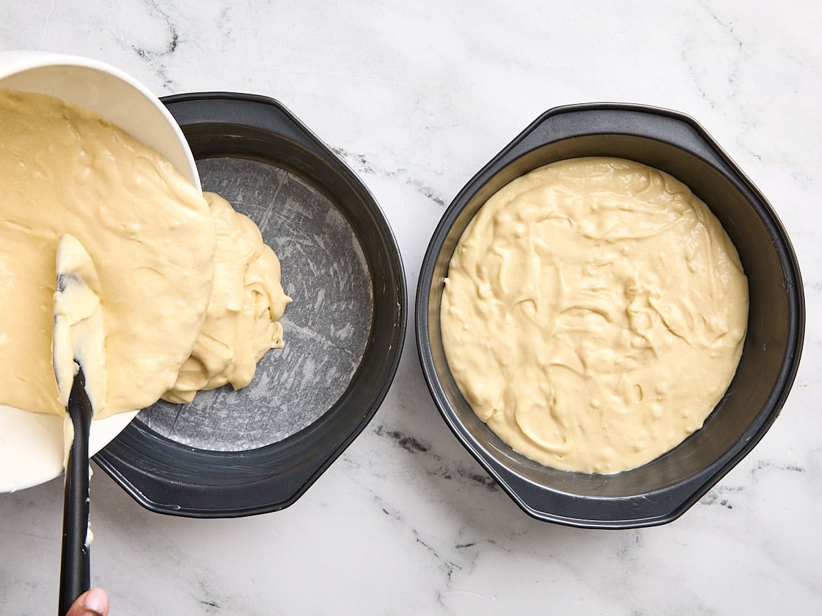 Coconut cake batter being poured into two cake pans.