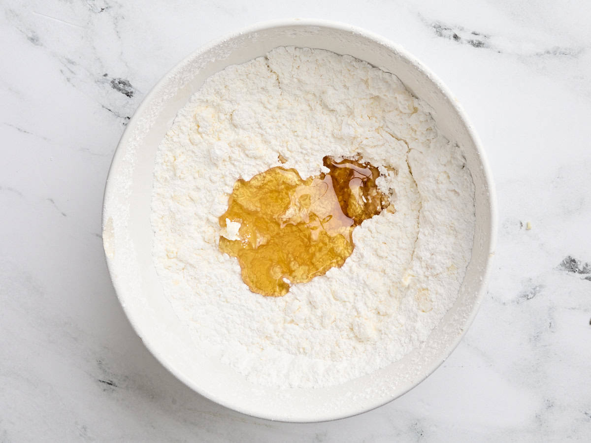 Honey and vanilla added to mixed powdered sugar and butter in a bowl.
