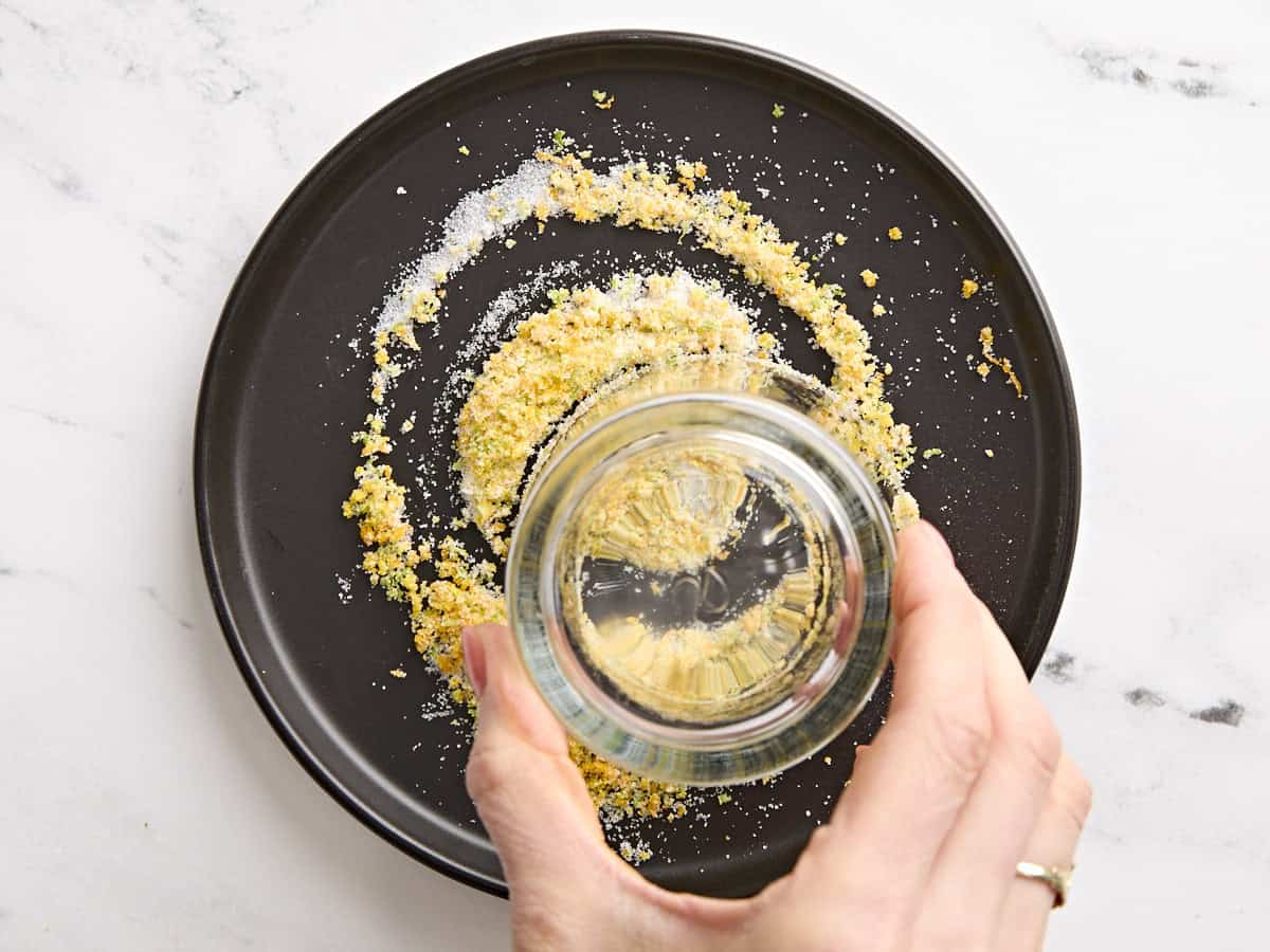 The rim of a rocks glass being pressed into a salt, lime zest, and orange zest mixture to rim the glass.