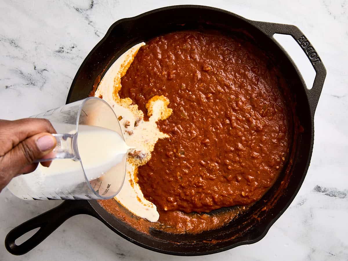 Heavy cream being added to a skillet to make a homemade butter chicken sauce.