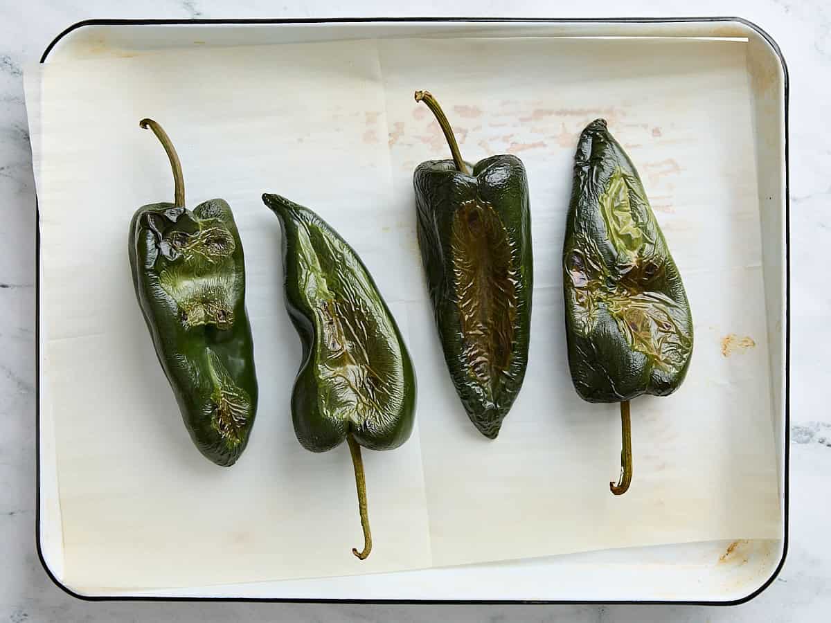 Finished roasted poblano peppers on a parchment lined baking sheet.