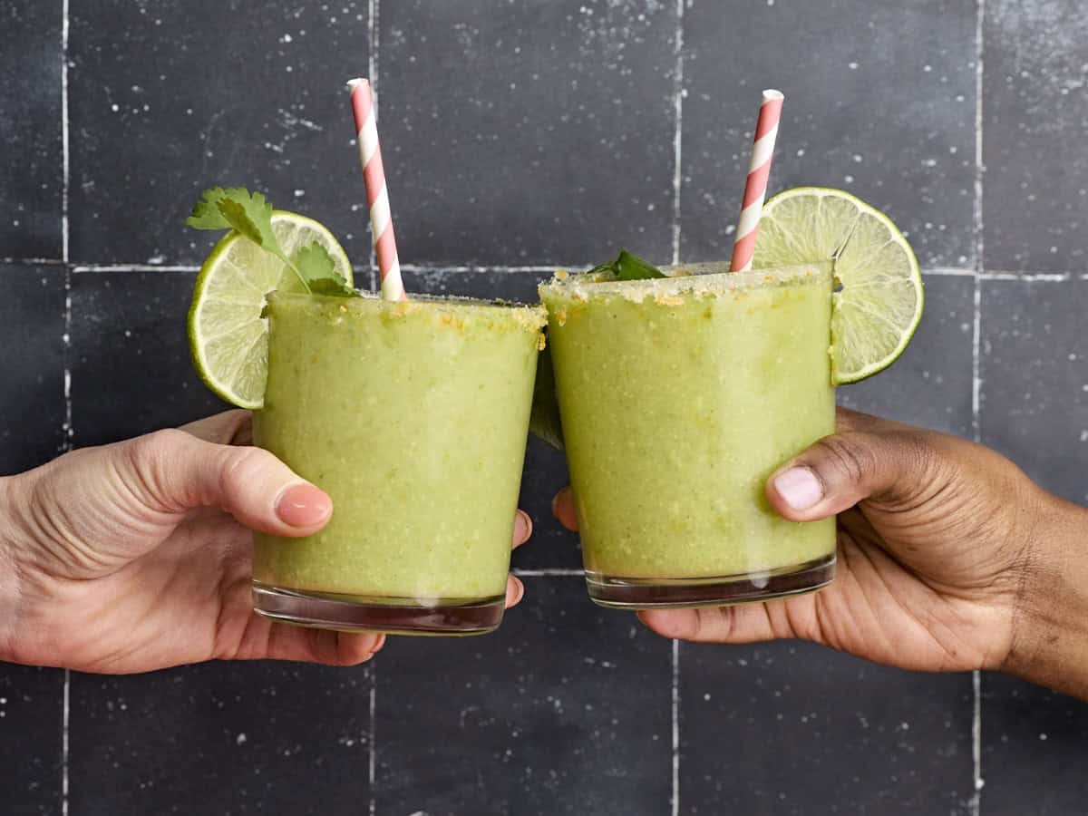 Two hands clinking together two glasses of homemade avocado margarita