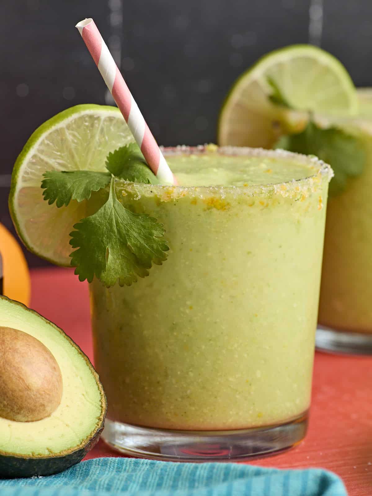 Side view of a glass of avocado margarita, garnished with lime slices and fresh cilantro.