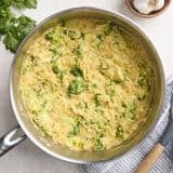 Overhead view of creamy broccoli cheddar orzo in a skillet.