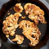 Overhead view of cauliflower steaks in a skillet.