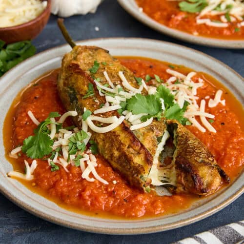 Side view of a homemade chile relleno on a plate with a slice though the end.
