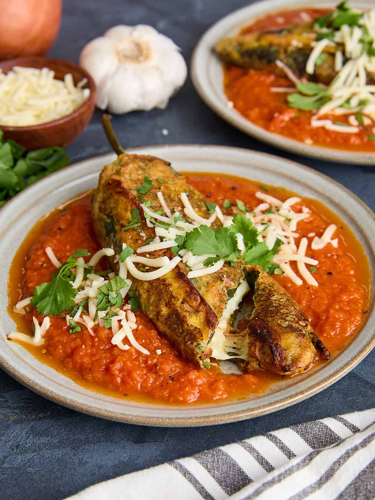 Side view of a homemade chile relleno on a plate with a slice though the end.