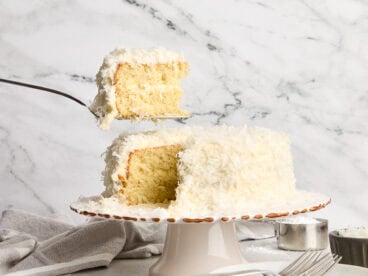 A piece of coconut cake being taken from a cake stand.