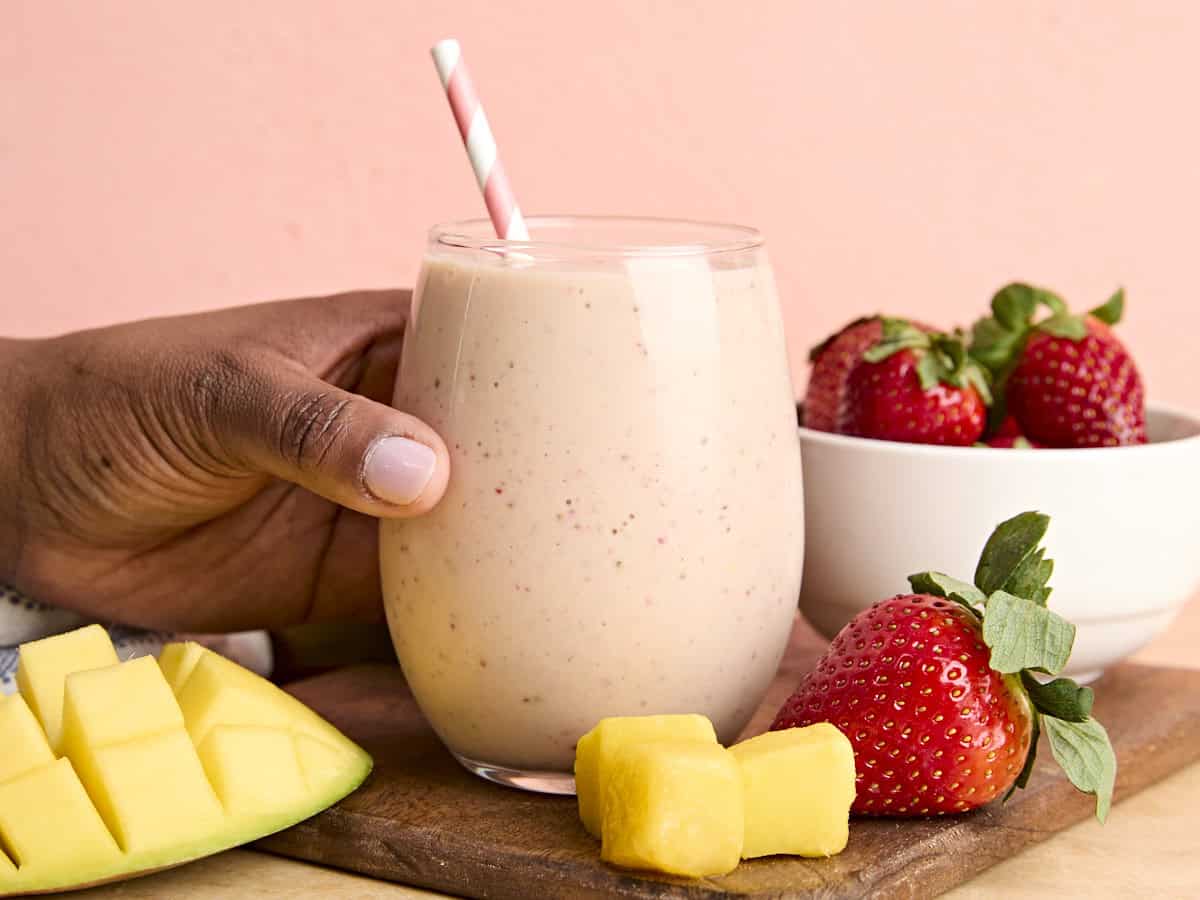 A hand hold a glass of strawberry mango smoothie.