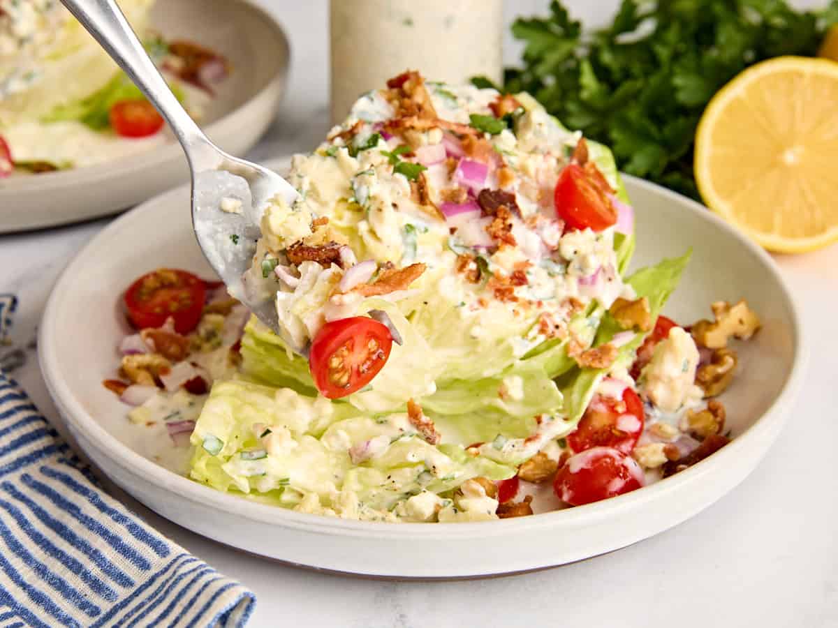 A wedge salad on a plate with some being taken with a fork.