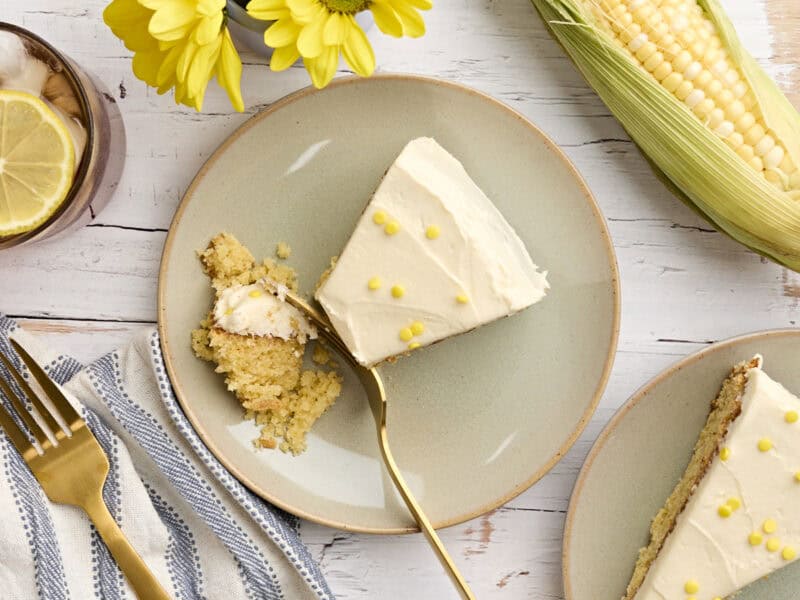 Overhead view of a homemade cornbread cake with honey buttercream frosting on a plate with a fork taking some.