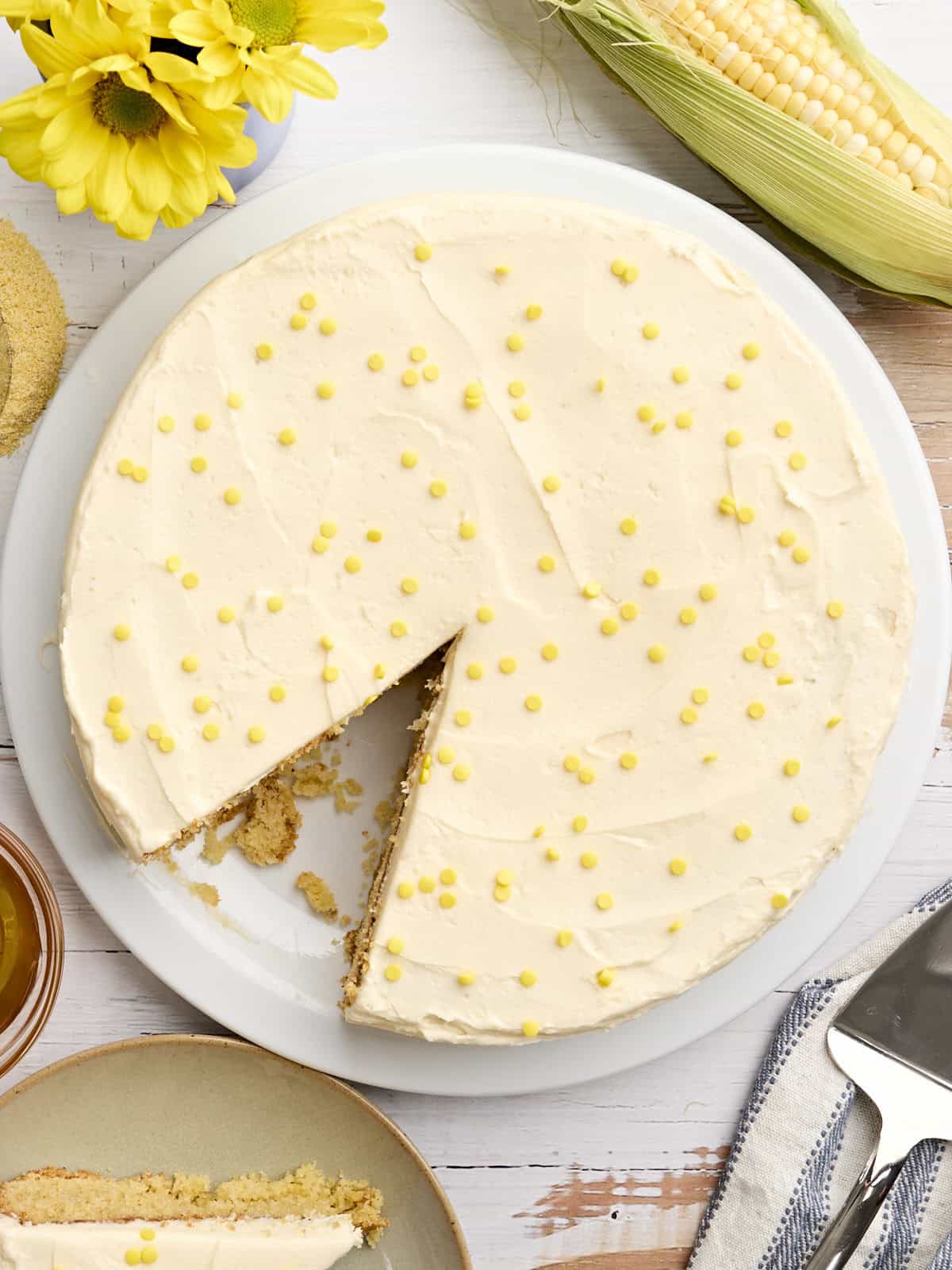 Overhead view of a cornbread cake with honey buttercream frosting, topped with yellow sprinkles.