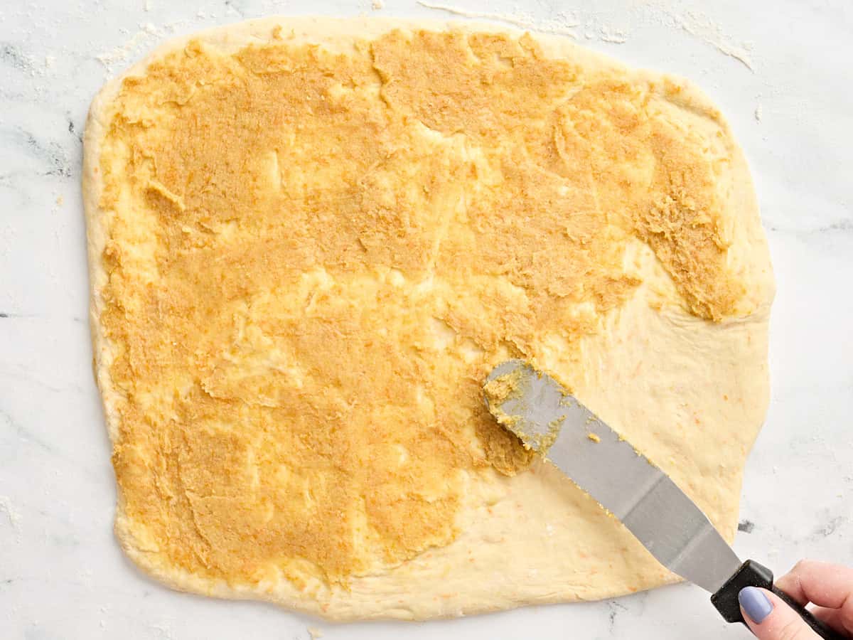 Homemade orange roll filling being spread over homemade dough.