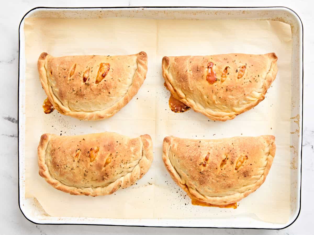 Four freshly baked homemade calzones on a parchment lined baking sheet.