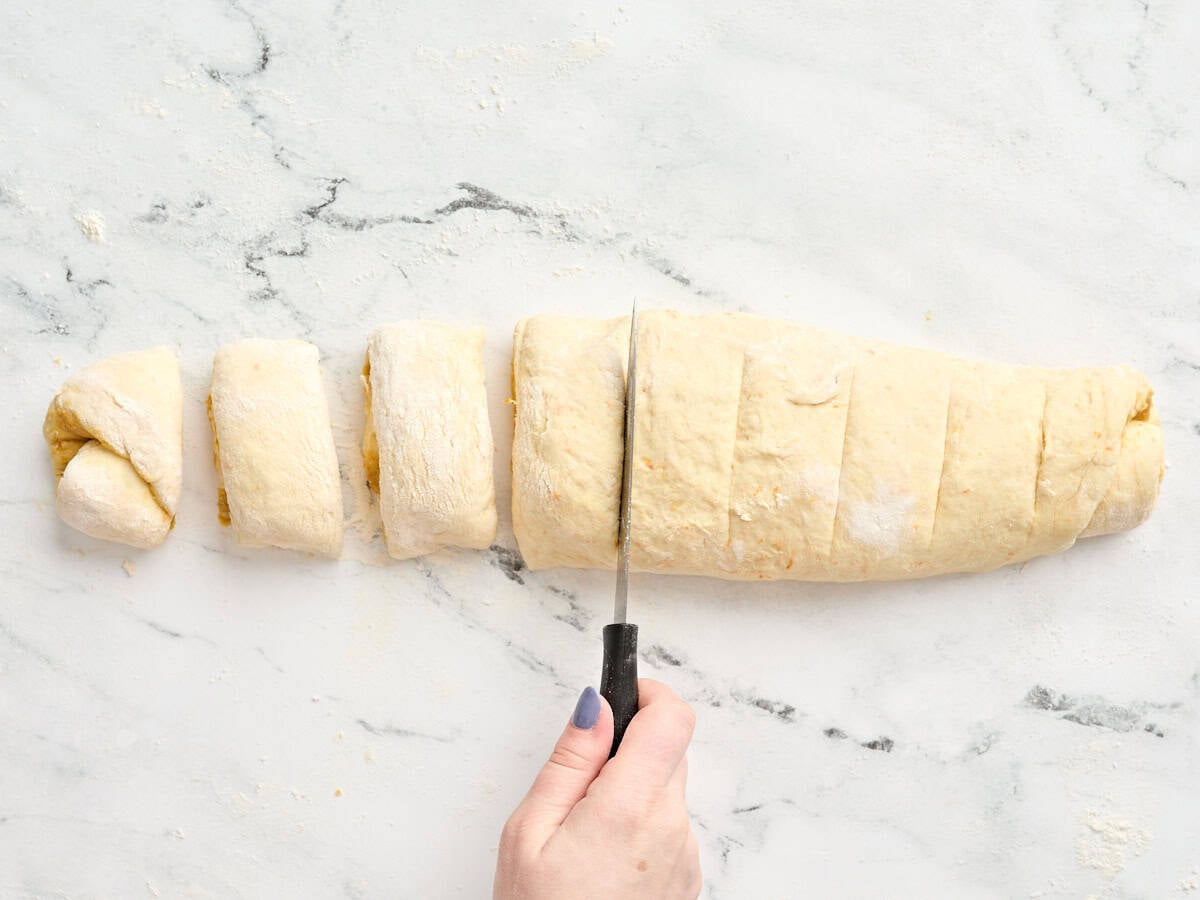 A knife slicing the rolled dough into individual slices.