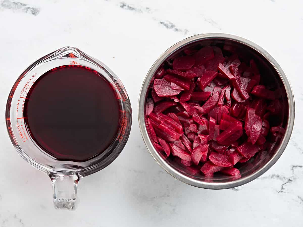Canned beets in a sauce pan with the juice from the can in a second jug.