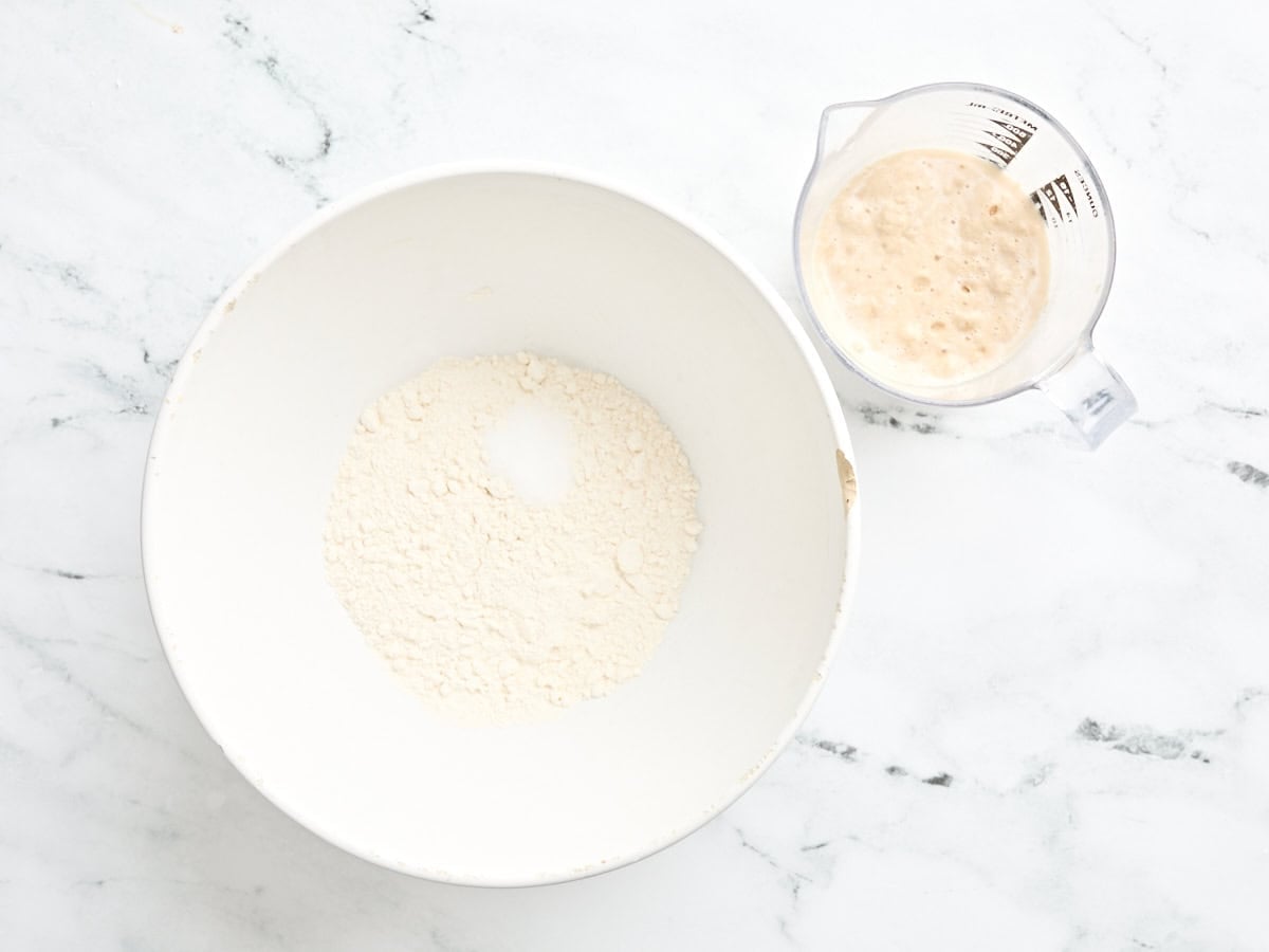 Yeast and warm water in a glass measuring just, next to a bowl of flour.