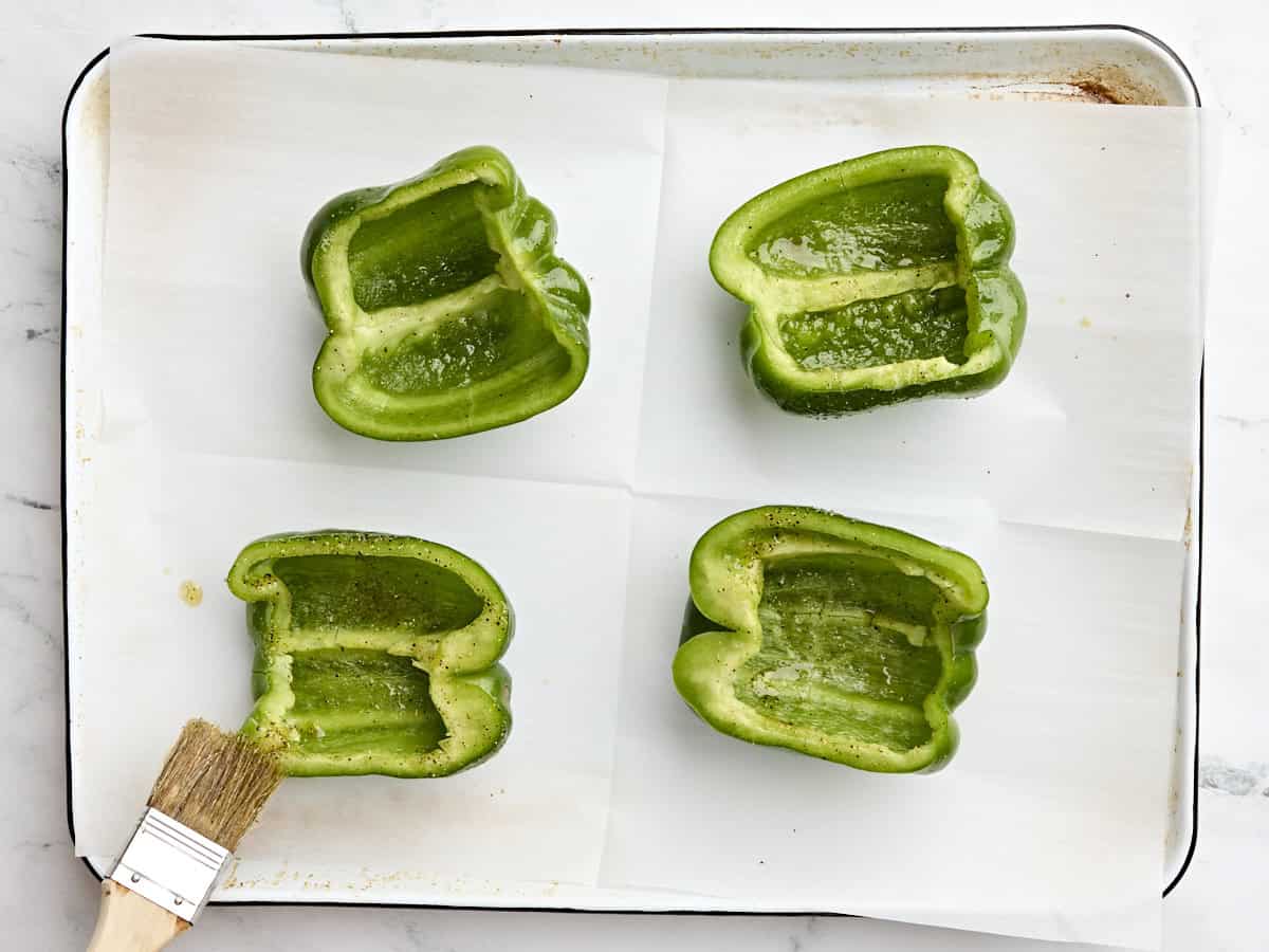 Green bell pepper halves being brushed with oil.