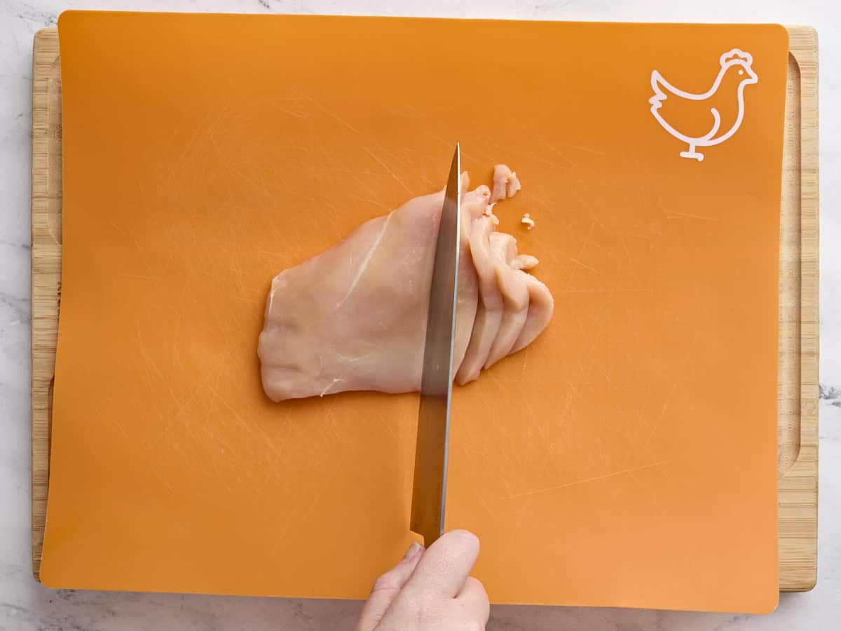 A chicken breast being sliced on a cutting board.