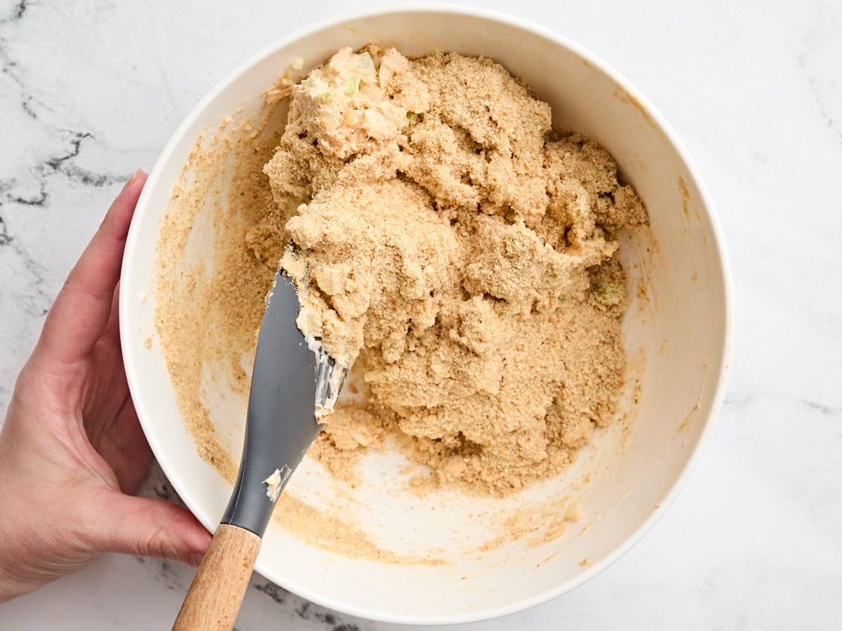 Crab cake mixture being mixed with a spatula in a mixing bowl.