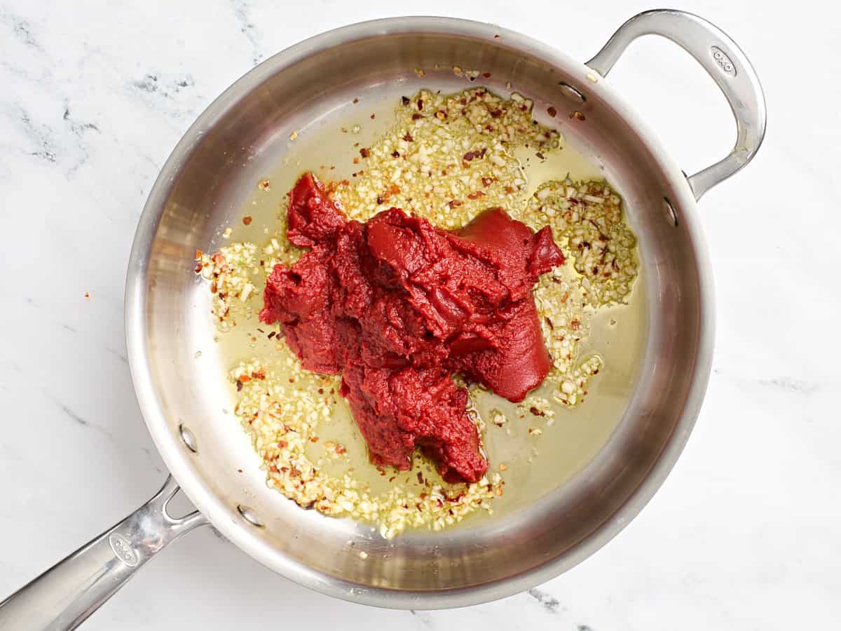 Tomato paste added to a skillet with minced garlic and red pepper flakes.