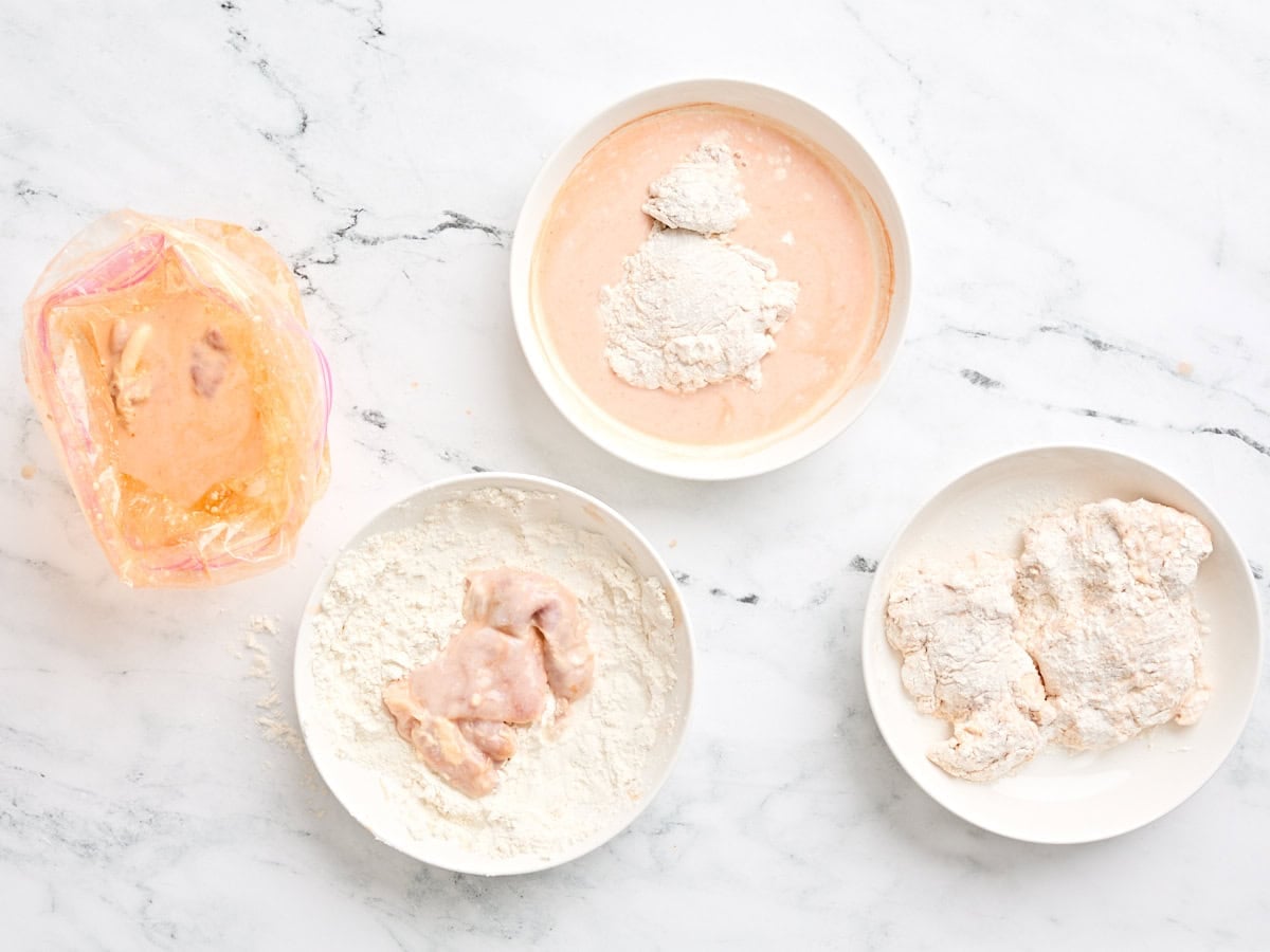 Overhead view of marinated chicken being dipped in a flour mixture and then placed on a separate bowl.