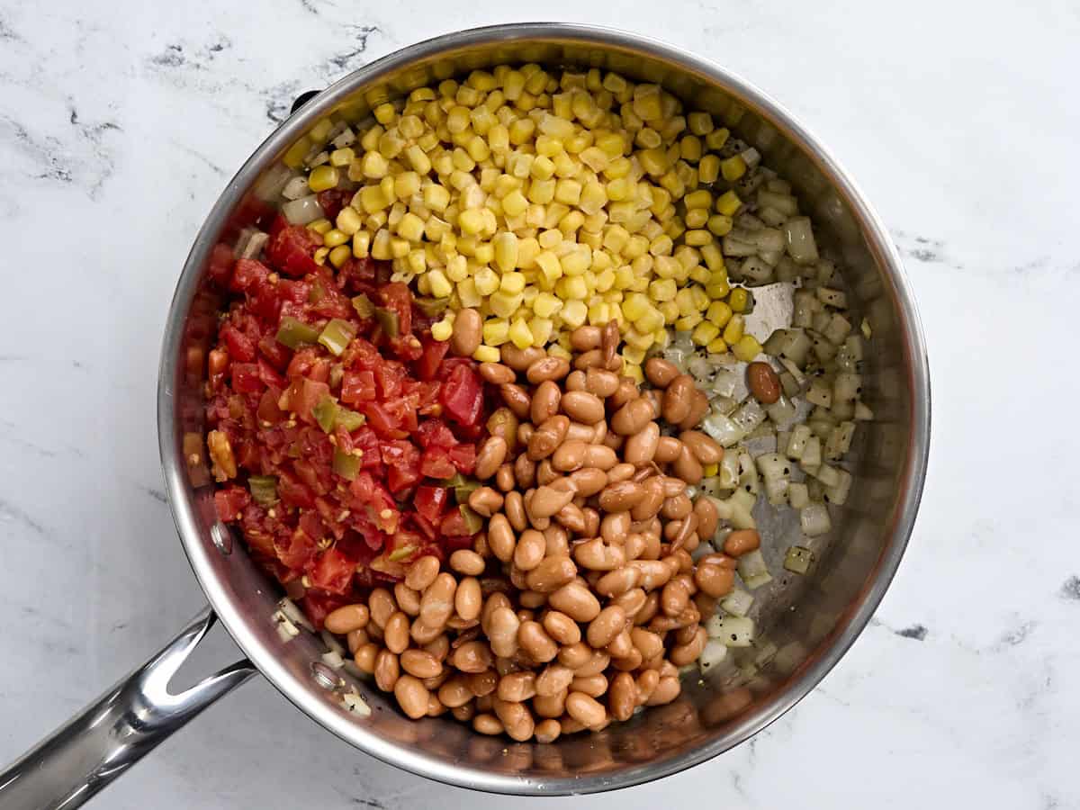 Diced tomatoes, corn, and beans added to sauteed onions in a skillet.