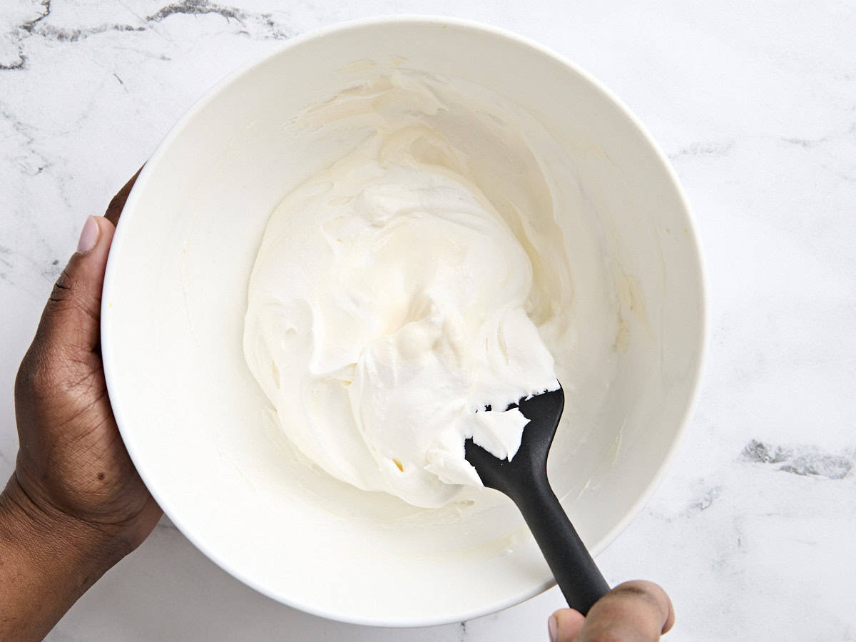 A spatula mixing the ingredients together for fruit dip in a bowl.