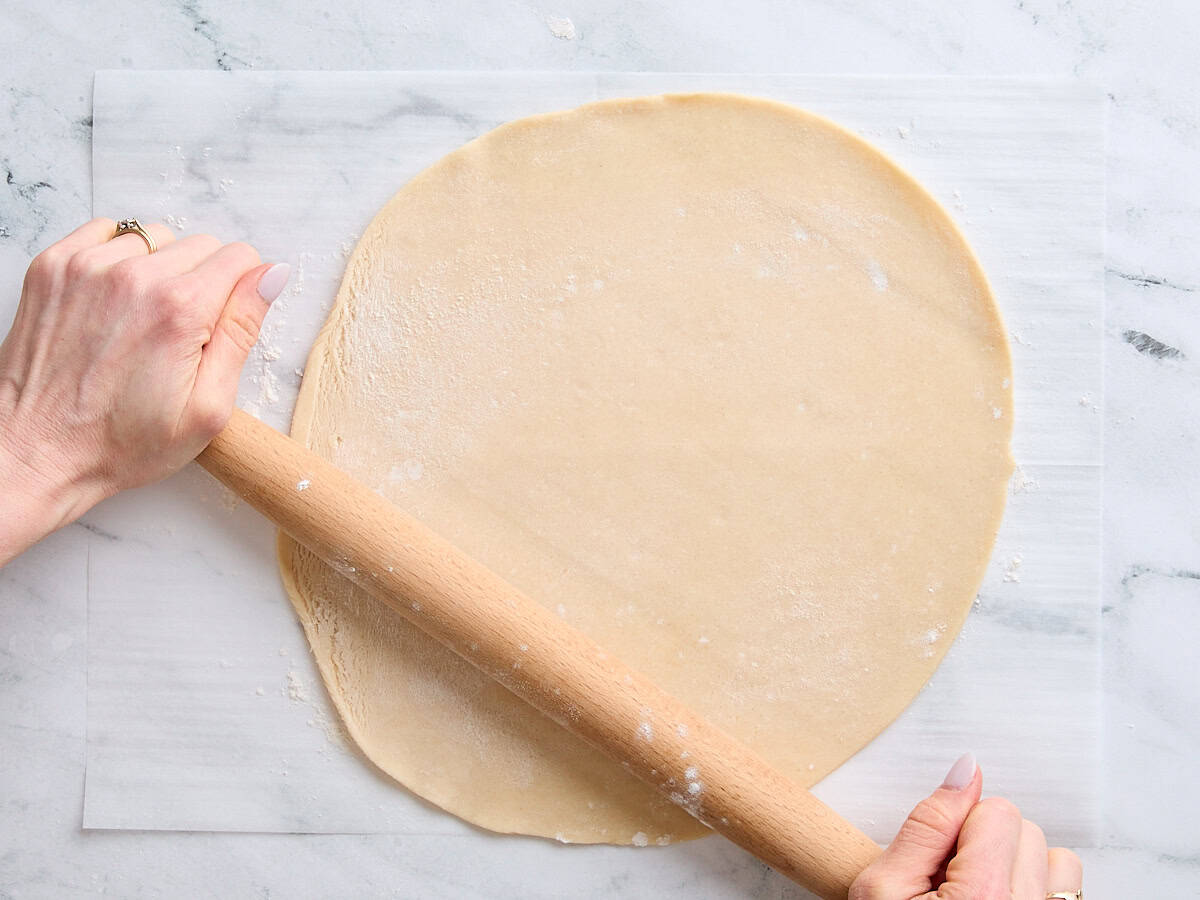 Hands using a rolling pin to roll out a pie crust.