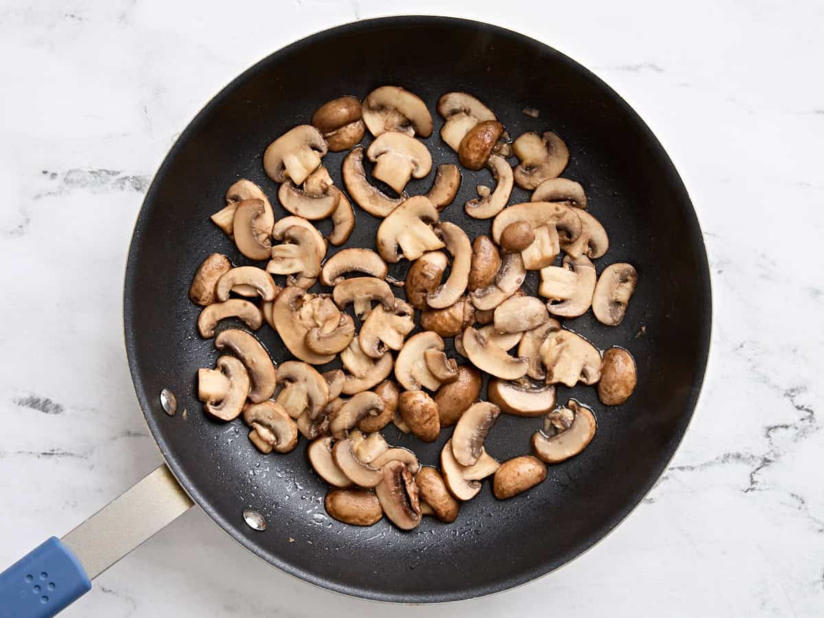 Mushrooms sauteeing in a skillet.