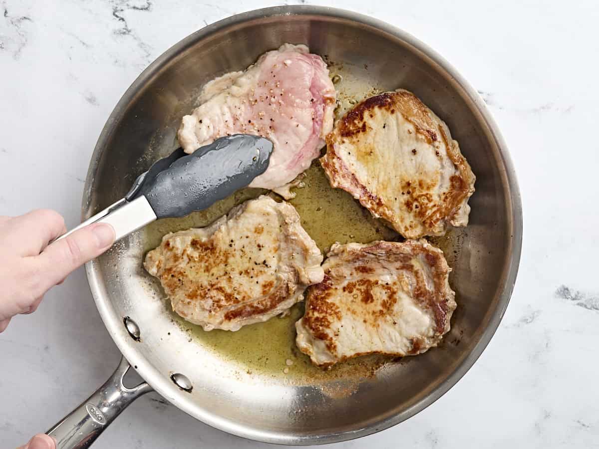 Four pork chops cooking in a skillet.