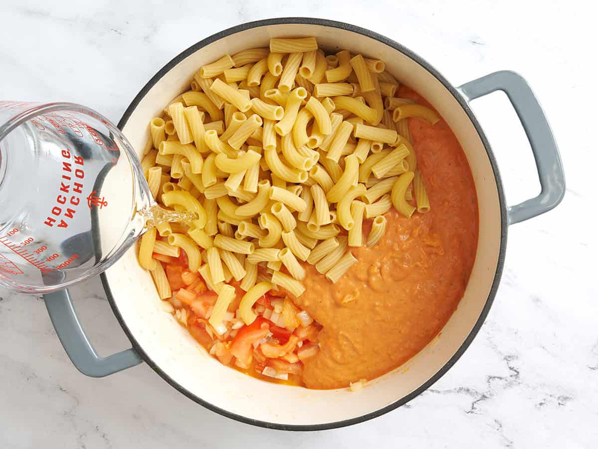 Vodka sauce and dried pasta added to sauteed onions and tomatoes in a pot.