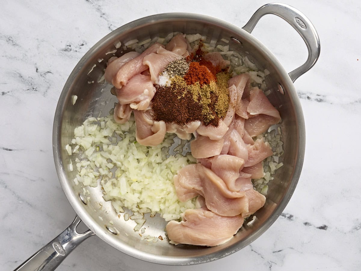 Sliced chicken breast and seasonings added to sauteed onions and garlic in a saute pan.