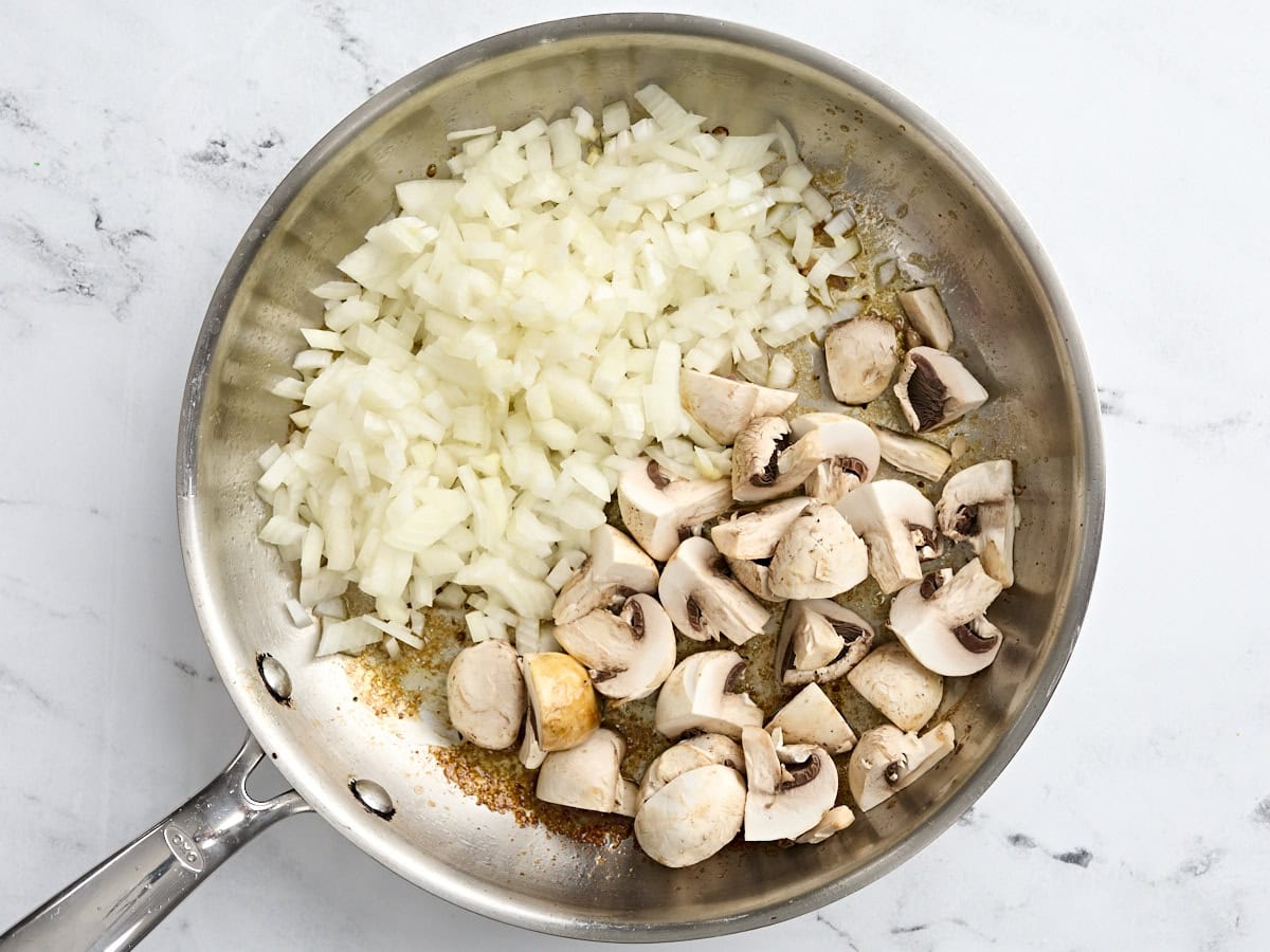 Sliced mushrooms and diced onion in a skillet.