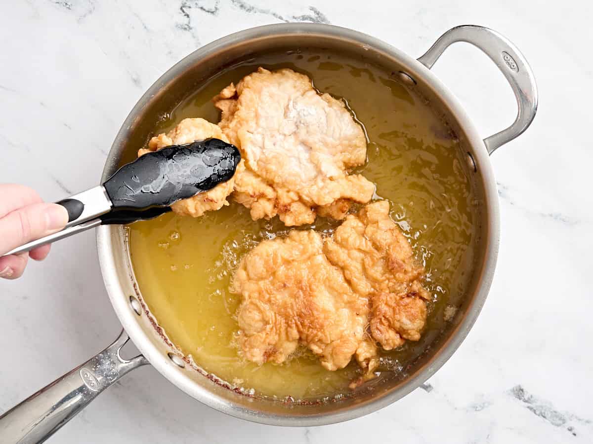 Breaded chicken frying in hot oil in a skillet.